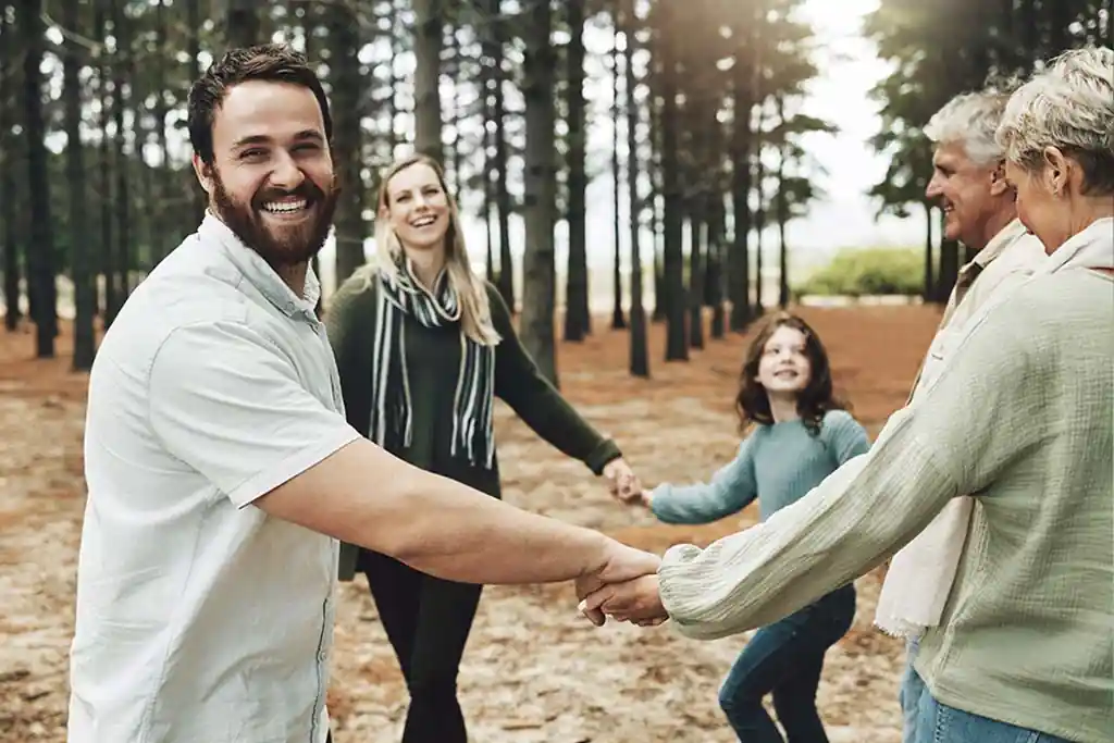 Família de várias gerações de mãos dadas em bosque, ilustrando apoio familiar na recuperação