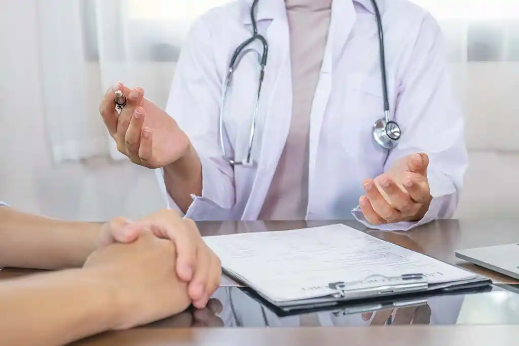 Profissional de saúde com estetoscópio orientando familiar em consulta, com documentos sobre a mesa